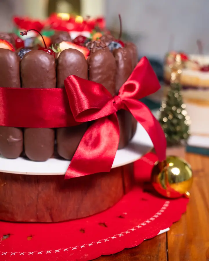 Bolo Charlotte de chocolate cercado de biscoitos e amarrado com laço de fita vermelha, decorado para o Natal
